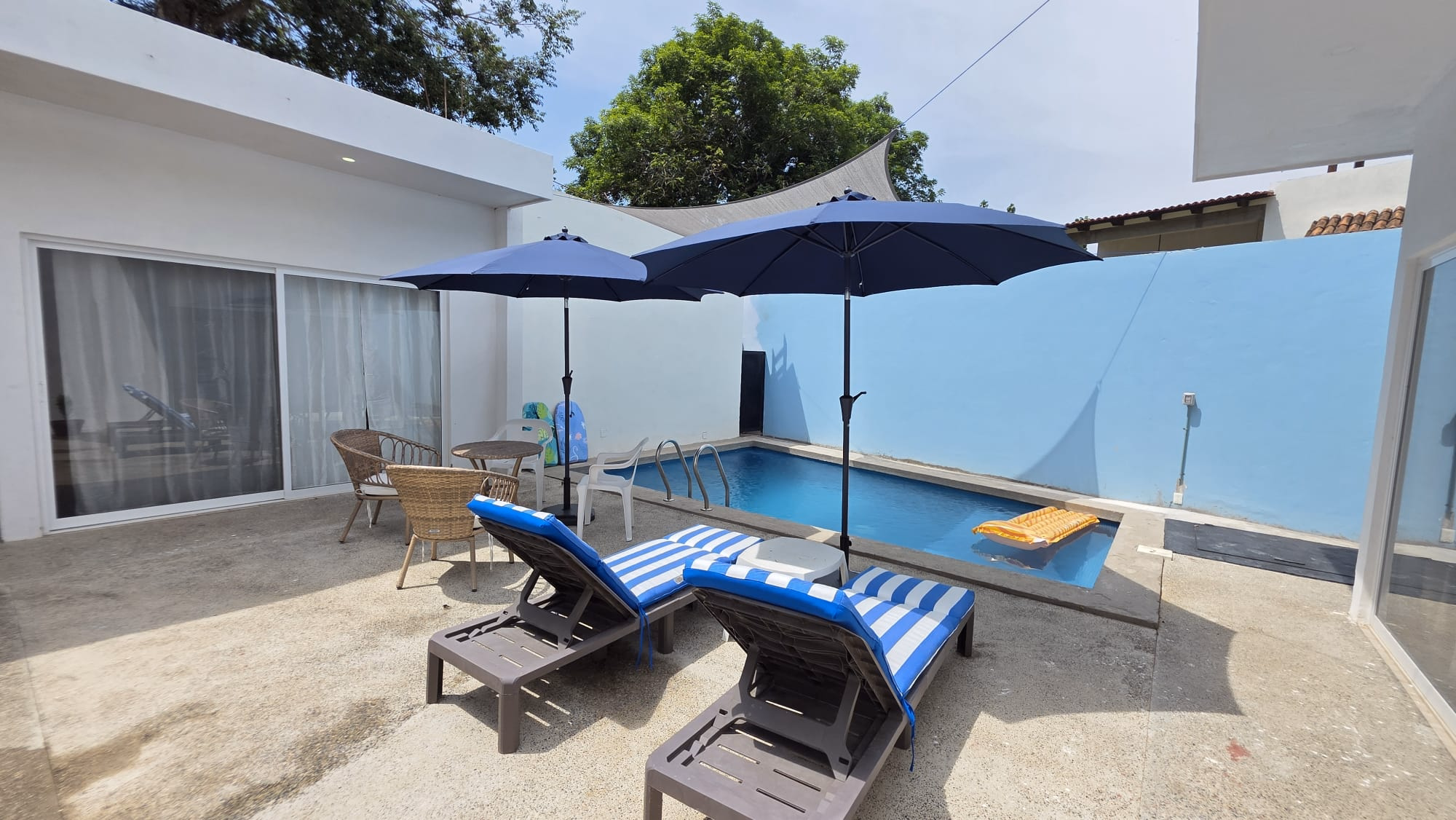 Casa Taya for sale in Sayulita, Nayarit, Mexico, featuring a modern single-story home with white and blue exterior, spacious parking area, and mature tropical trees.